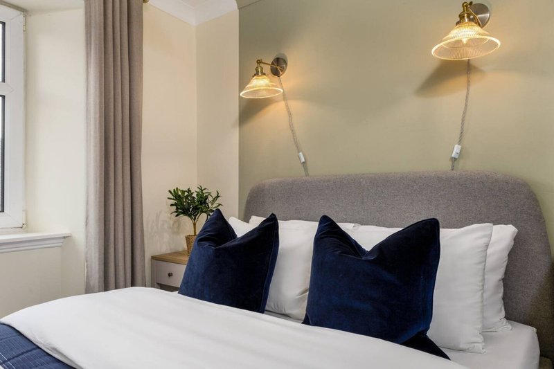 Modern bedroom with gray upholstered headboard, dark blue cushions, white bedding, brass wall lights