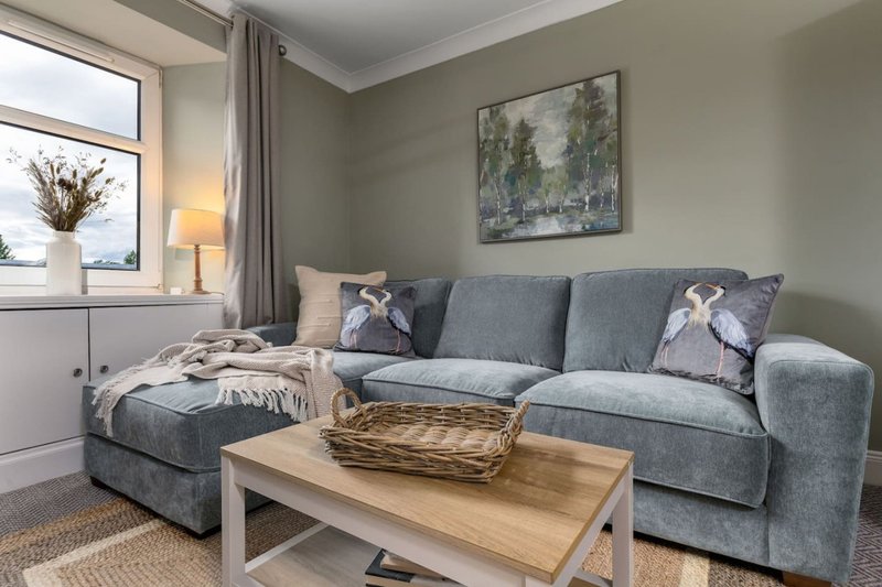 Modern living room with grey sofa, wooden coffee table, cushions and landscape artwork