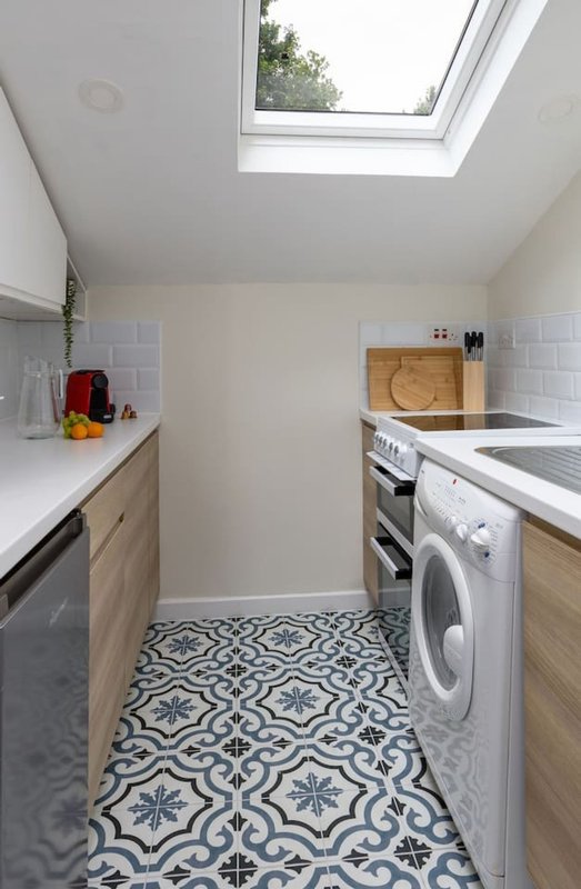 Modern galley kitchen with white counters, wooden cabinetry, washing machine and skylight