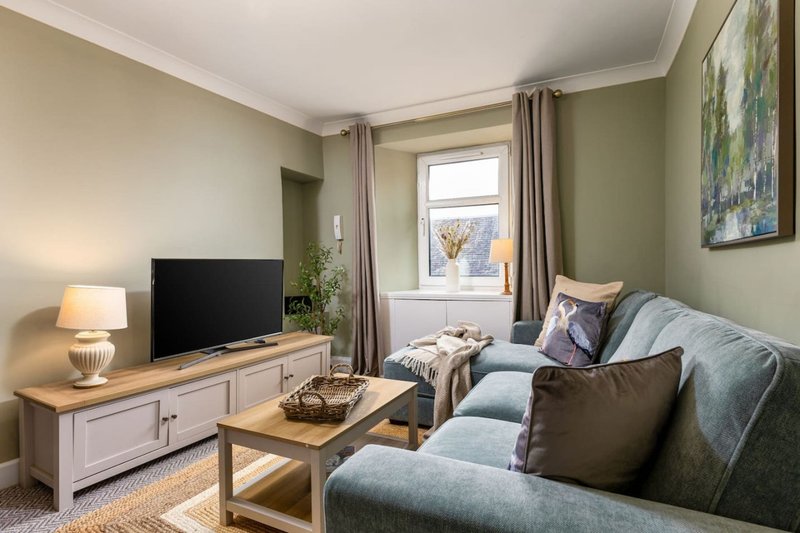 Living room with sofa, TV unit, coffee table, lamp, and window view