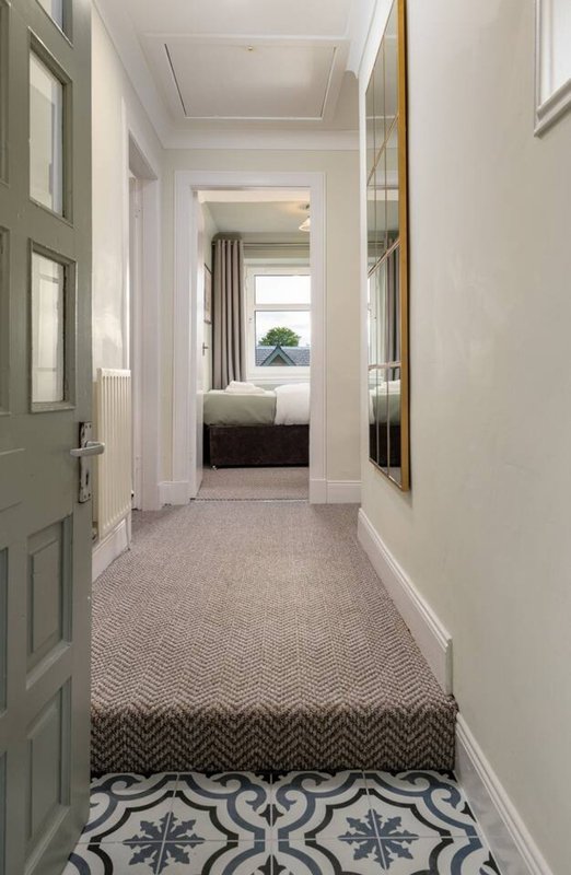 Long hallway with patterned tile floor, cream walls, and view through to bedroom