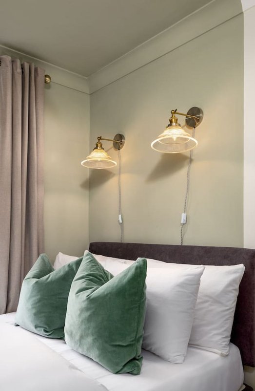 Bedroom with double bed, green and white pillows, wall-mounted pendant lamps, curtains