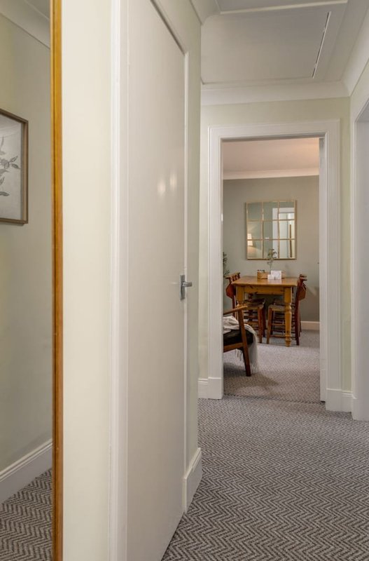 Bright hallway with white walls, gray carpet, and open doorway to dining area