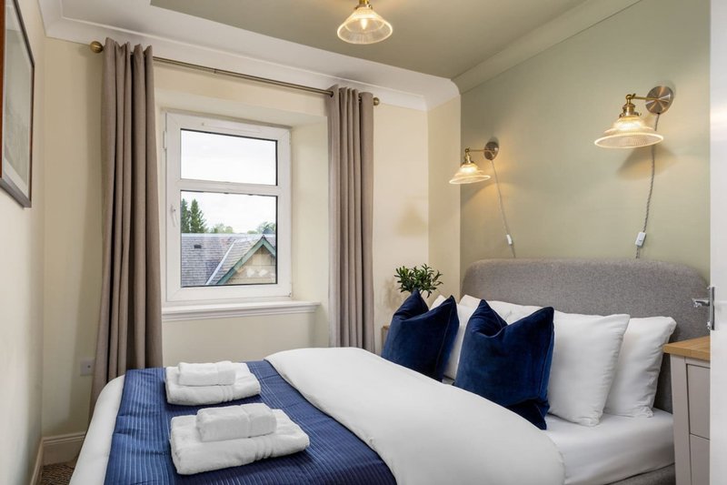 Bright bedroom with double bed, blue and white bedding, window with curtains, wall sconces