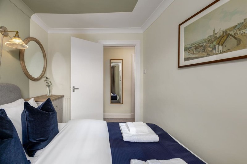 Compact bedroom with single bed, navy bedding, round mirror and framed landscape artwork