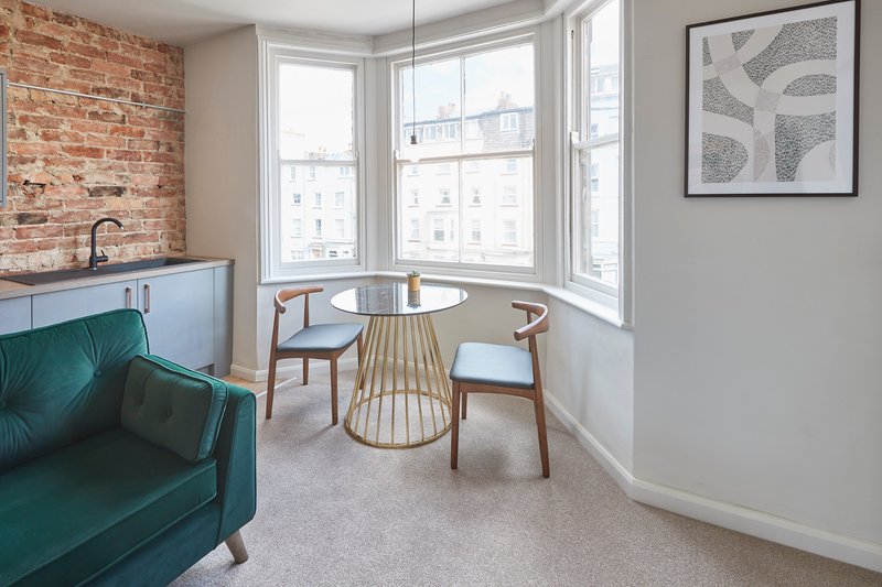Modern living room with teal sofa, dining table, bay windows and exposed brick wall