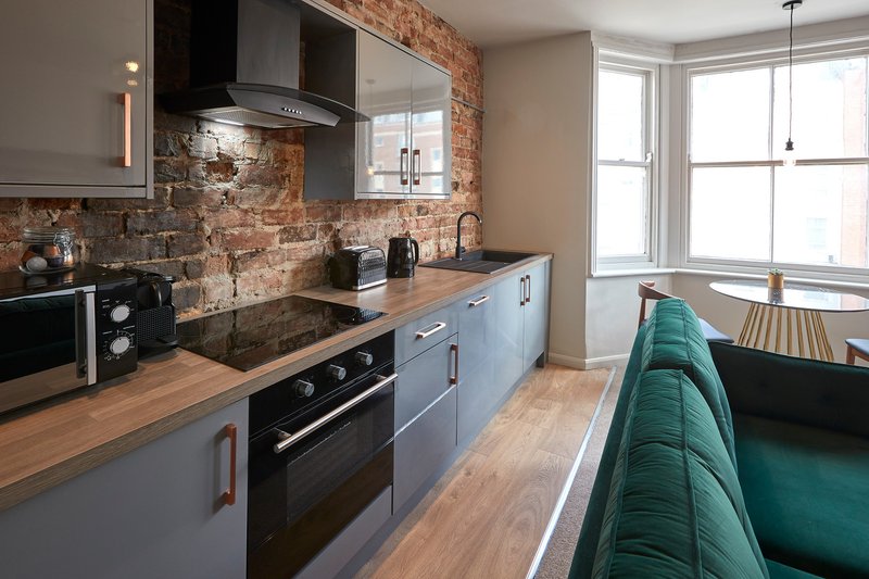 Modern kitchen with blue cabinetry, brick backsplash, wooden worktops and black appliances