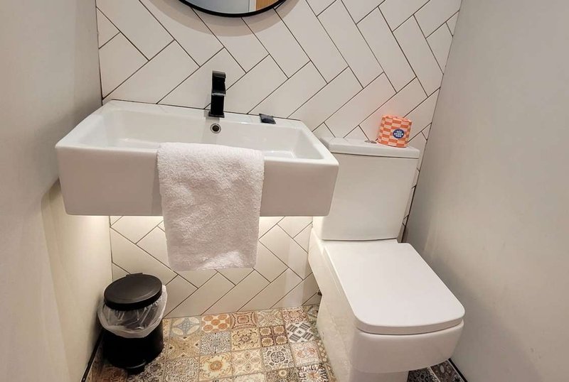 Modern bathroom with white sink, toilet, herringbone tile wall and patterned floor