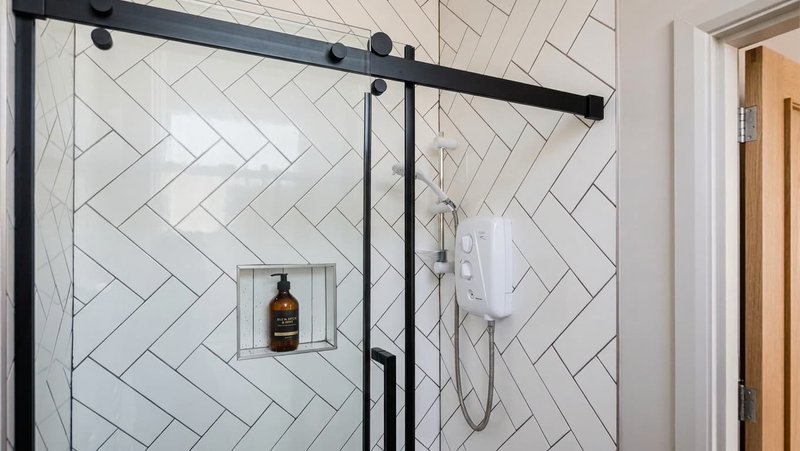 Modern bathroom shower with herringbone tile, black framing, and glass enclosure