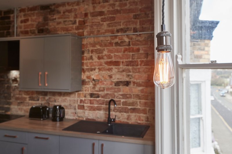 Modern kitchen with exposed brick wall, pendant light, sink and grey cabinetry