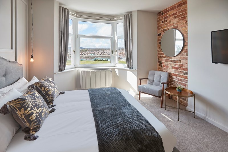 Modern bedroom with double bed, exposed brick wall, large bay window overlooking cityscape