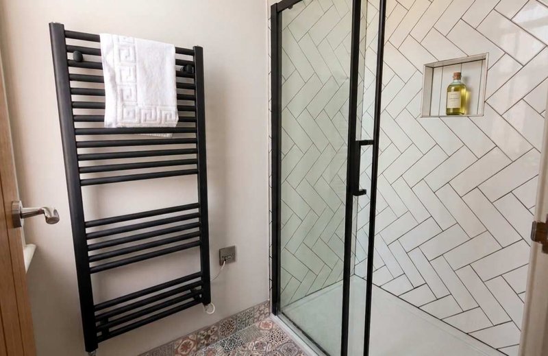 Modern bathroom with black heated towel rail, walk-in shower enclosure and herringbone tile pattern