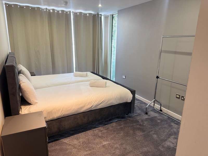 Modern bedroom with double bed, cream bedding, dark headboard, and floor-to-ceiling windows