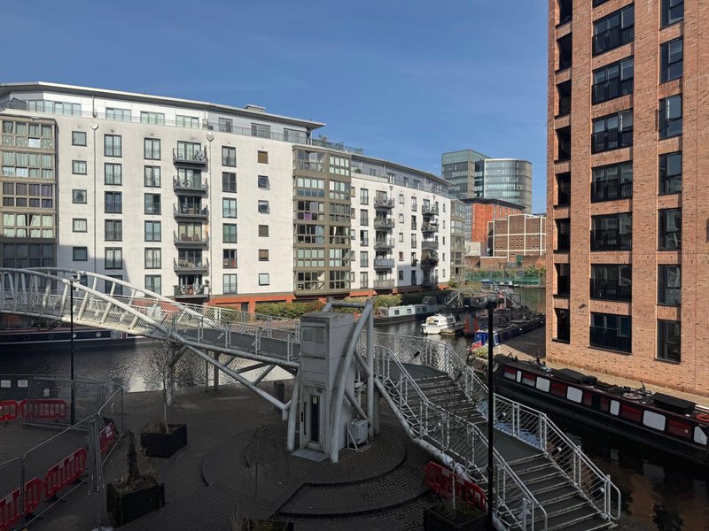 Urban apartment building exterior with modern balconies, waterside walkway and neighboring residential towers