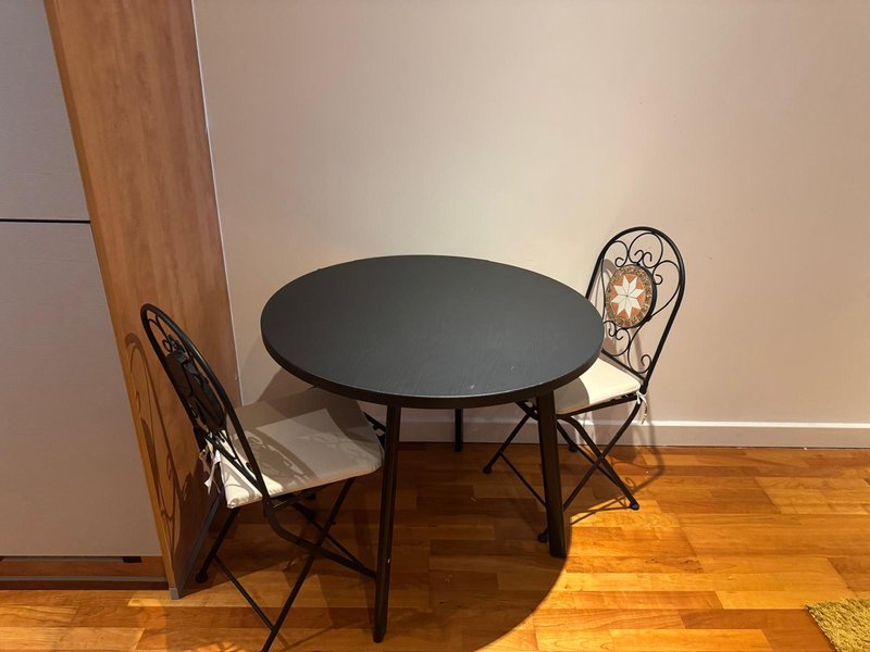 Dining area with round black table, two decorative metal chairs, wooden flooring