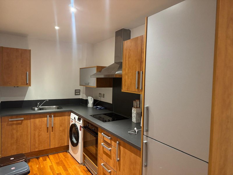Modern kitchen with wooden cabinets, black countertops, integrated appliances and stainless steel fridge