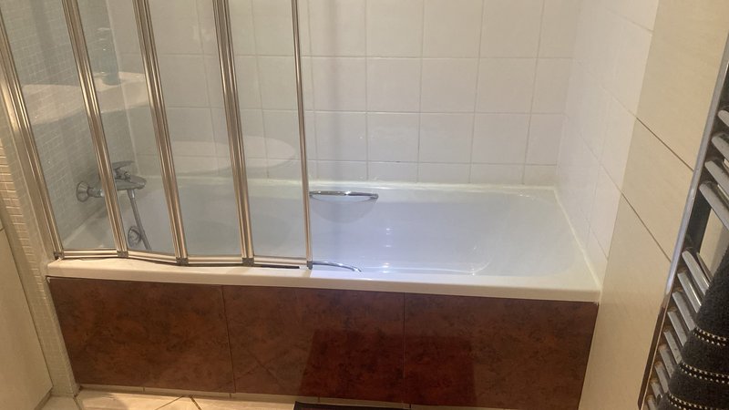 Bathroom with modern shower enclosure, white tile walls, and wooden bath panel
