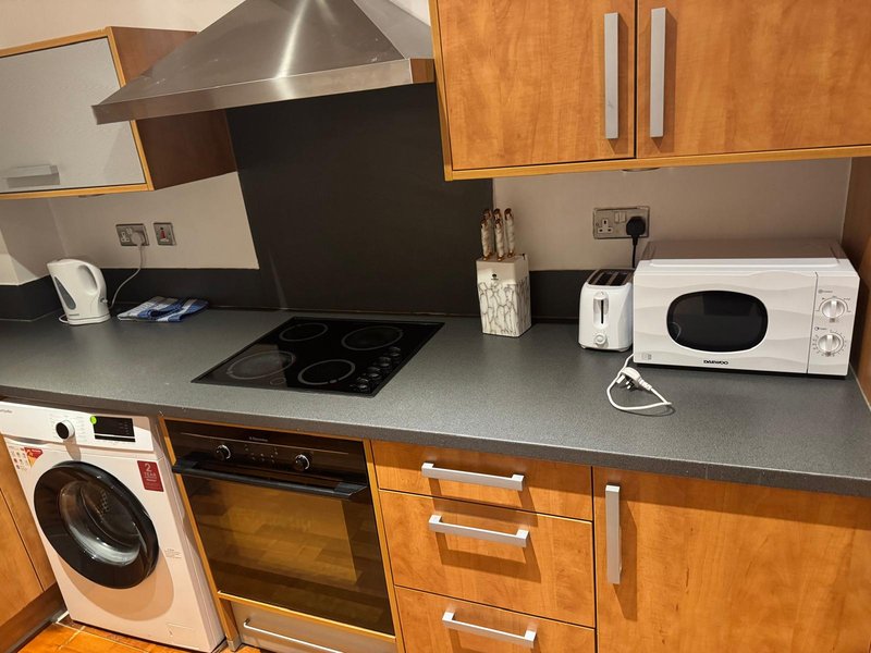 Modern kitchen with wooden cabinets, stainless steel cooker hood, induction hob, white washing machine and microwave