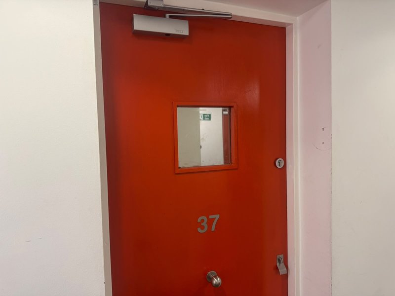 Red fire door numbered 37 with small window and metal fixtures