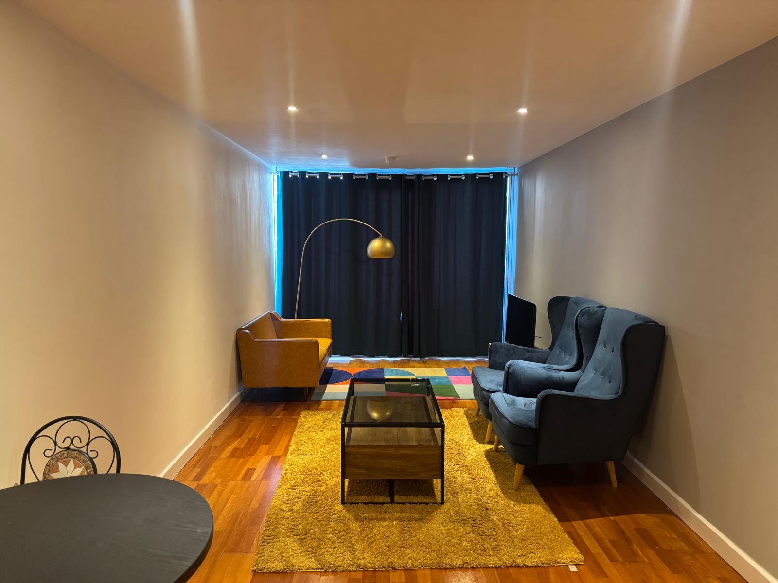 Modern living room with mustard yellow rug, black sofa, tan armchair, and arc floor lamp