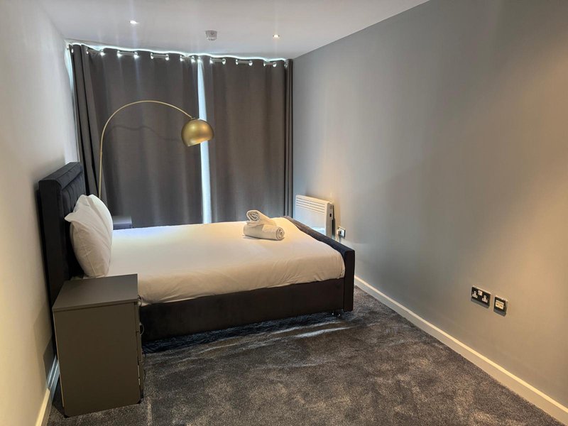 Modern bedroom with black bed frame, white pillows, arc lamp, dark curtains and grey carpet