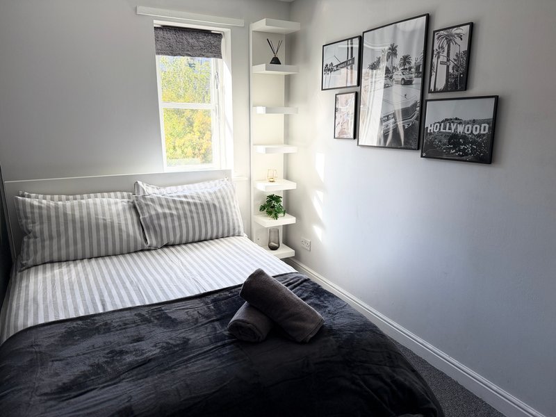 Compact bedroom with striped bedding, window, wall-mounted framed prints, and bedside plant