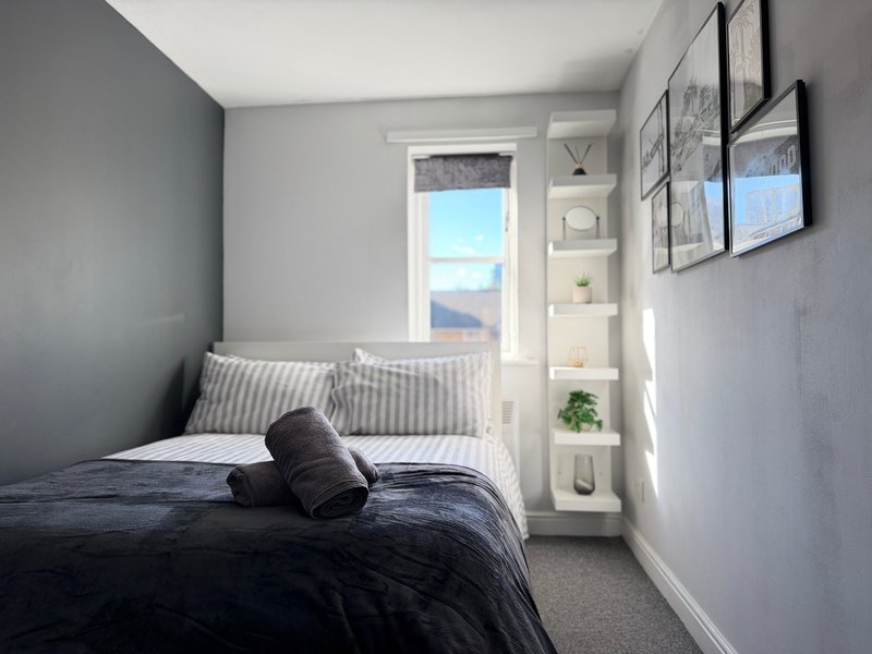 Compact bedroom with double bed, dark bedding, striped pillows, window with mountain view, and wall shelving