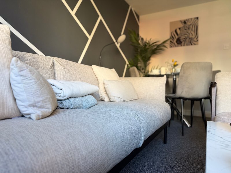 Modern living room with gray sofa, white pillows, geometric wall art, and potted plant