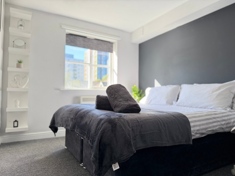 Modern bedroom with double bed, dark headboard, window with natural light, and built-in shelving