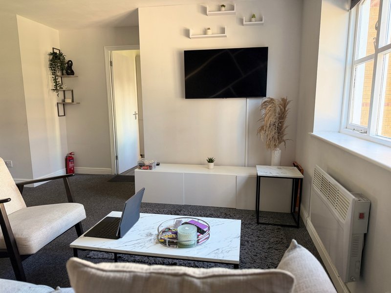 Modern living room with TV mounted on wall, white storage unit, beige armchairs and coffee table