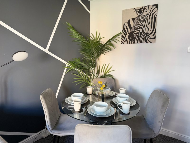 Modern dining area with round black table, place settings, potted plant and geometric wall art