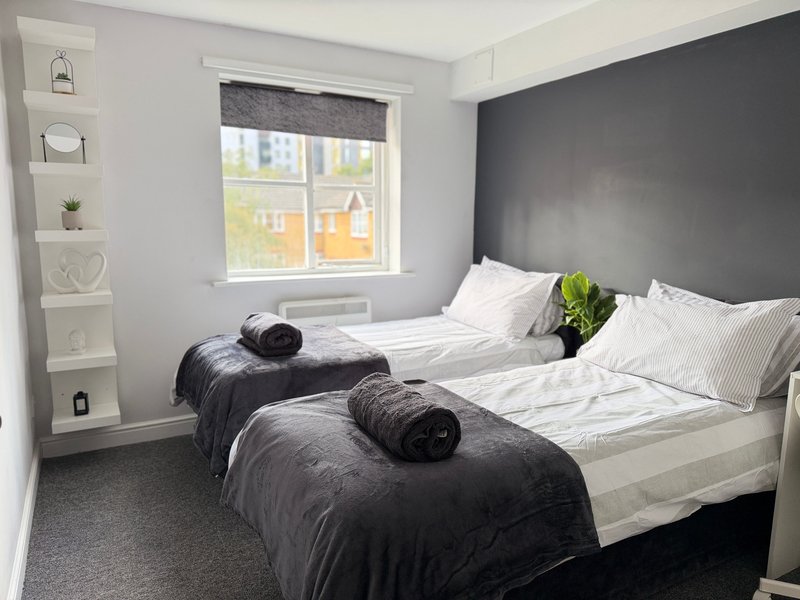 Modern bedroom with two single beds, dark headboard, white bedding, and window with city view, can also be a King Size bed as is a zip&link type.