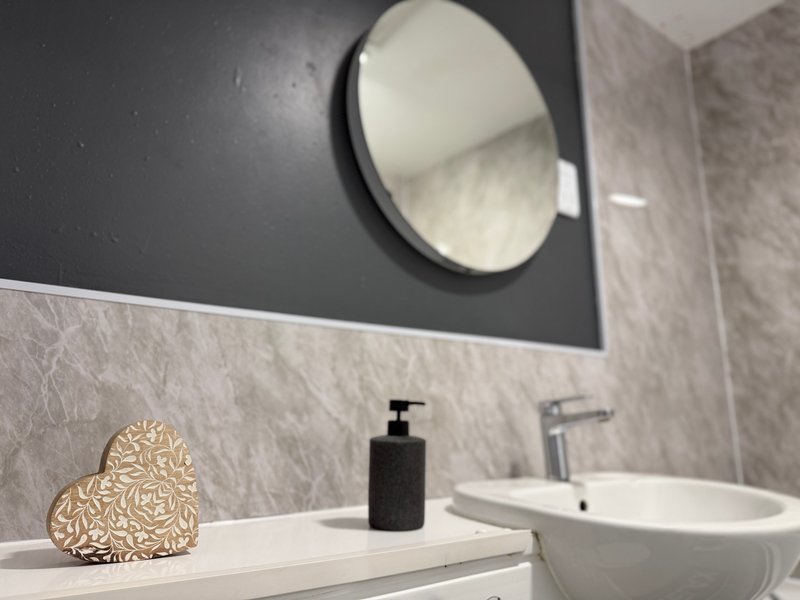 Modern bathroom with round mirror, white sink, black soap dispenser and decorative heart ornament