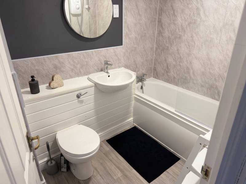 Modern bathroom with toilet, pedestal sink, bathtub, round mirror and grey tile walls