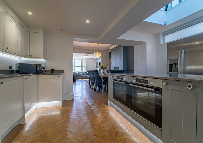Modern kitchen with white cabinetry, wooden herringbone flooring, stainless steel appliances and skylight