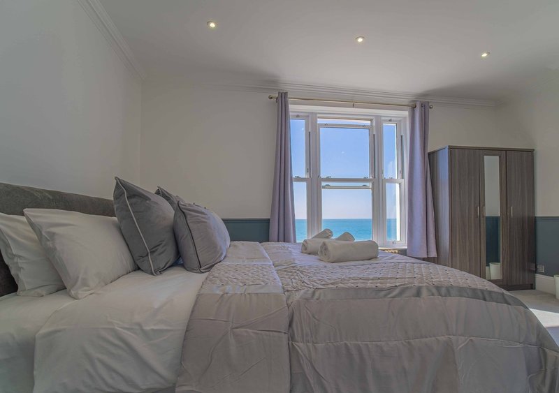 Bright bedroom with double bed, sea view through large window, purple curtains and wardrobe
