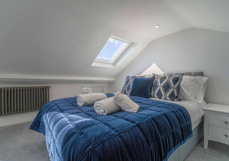 Modern attic bedroom with double bed, blue quilted bedding, rolled towels, skylight and radiator