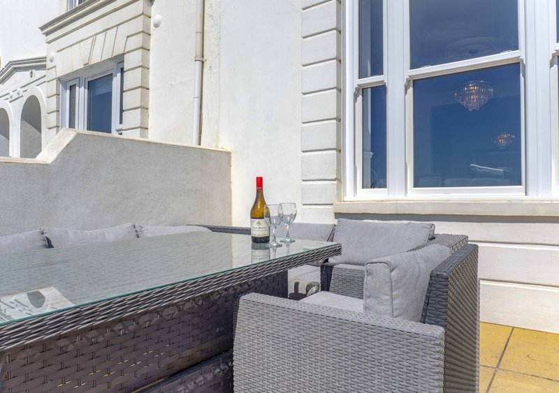 Outdoor patio seating area with wicker chairs, table, wine bottle and classical building facade
