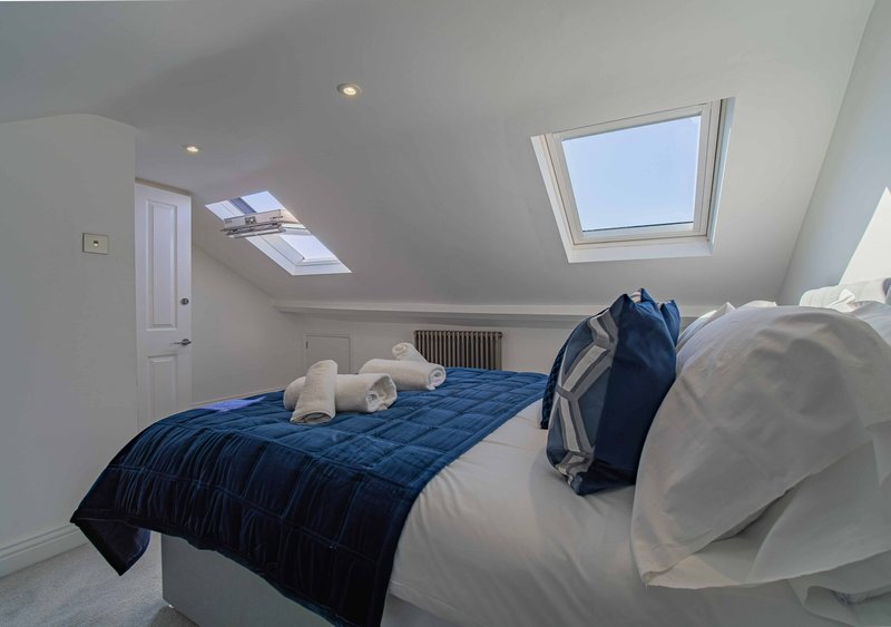 Bright attic bedroom with double bed, blue quilt, white pillows and skylight windows