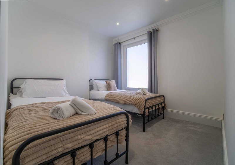 Bright bedroom with two single beds, metal frames, striped bedding and window with curtains