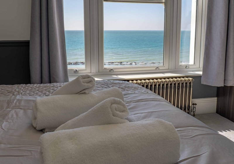 Bright bedroom with sea view, double bed, rolled towels and large windows overlooking beach
