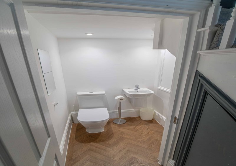 Compact bathroom with toilet, pedestal sink, wooden herringbone floor and white walls