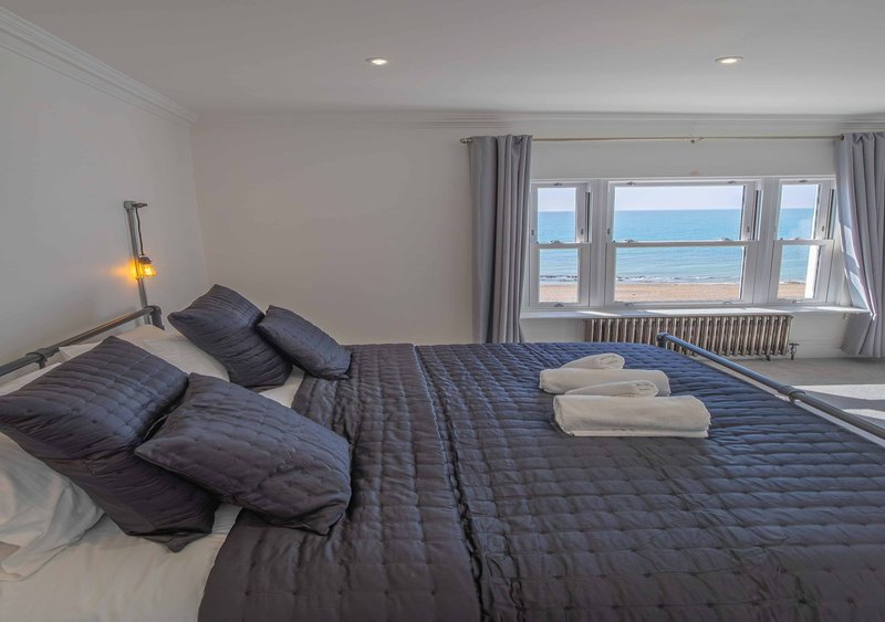 Bright bedroom with double bed, sea view through large windows, and modern minimalist decor
