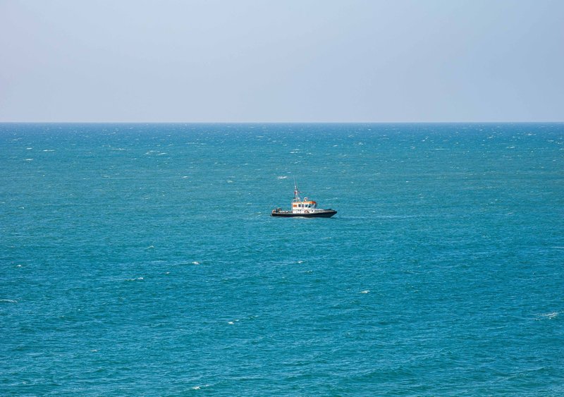 View of turquoise sea with small fishing or work boat on horizon