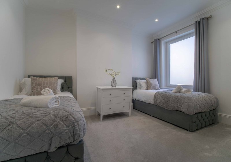 Twin bedroom with two beds, white dresser, flowers in vase, and large window with curtains