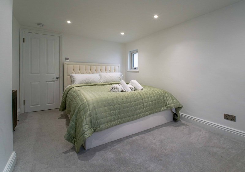 Bedroom with double bed, cream headboard, green quilt, fitted wardrobes and recessed lighting