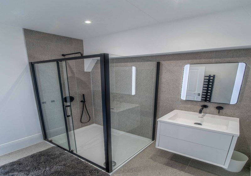 Modern bathroom with walk-in shower enclosure, white vanity sink and illuminated mirror