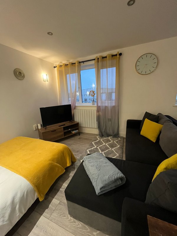 Studio bedroom with yellow bedding, black sofa, TV stand and large window with city views