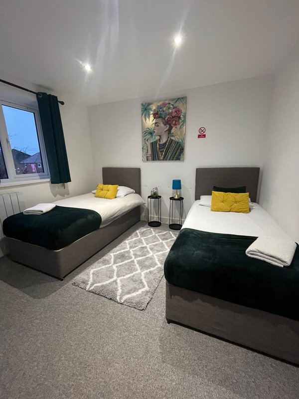 Twin bedroom with two single beds, yellow cushions, artwork, window with dark curtains