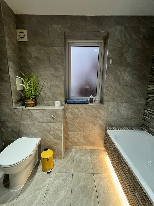 Modern bathroom with toilet, bathtub, window, potted plant and grey tile walls